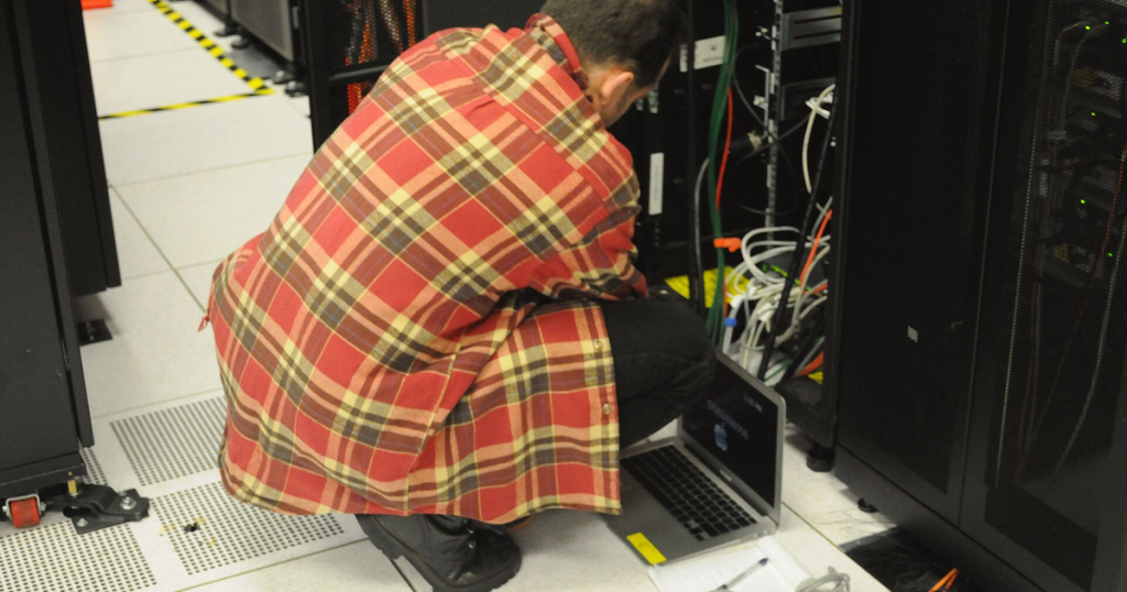 Technician working with a laptop beside a server rack in a data center